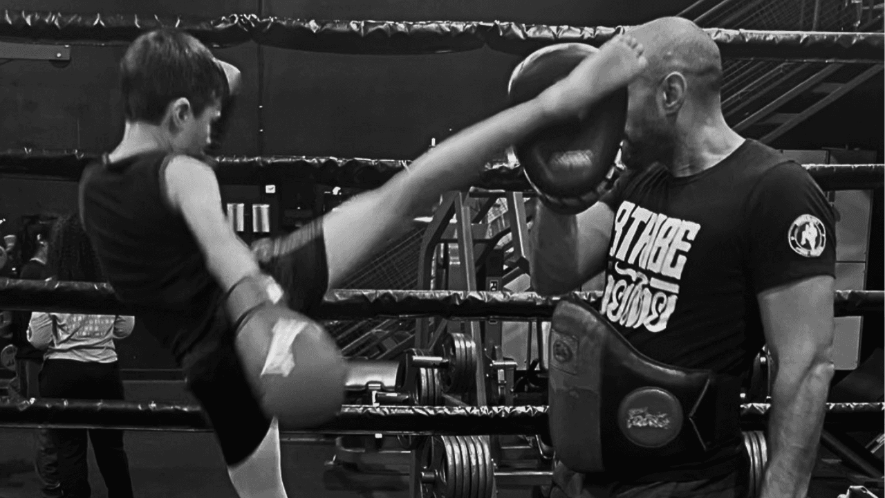 Young student throwing a high roundhouse into Thai pads